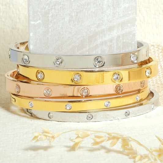 Elegant stainless steel bangle with a sleek push-lock design and polished finish, available in gold, rose gold, and silver, perfect for everyday wear, effortless stacking, and styling with watches.